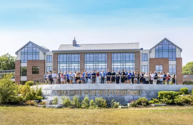 College of Business students and faculty stand in front of the UNE Commons on the Biddeford Campus